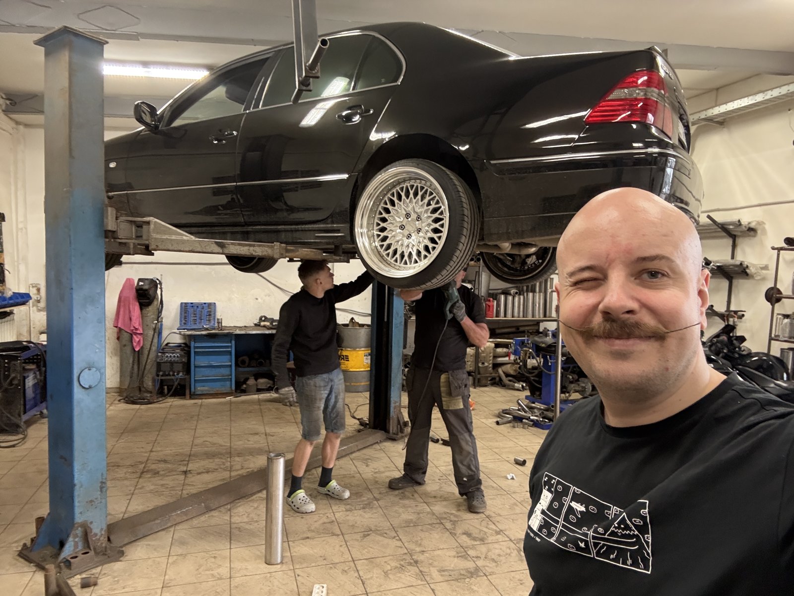 Чёрный Lexus LS430 на подъёмнике в боксе «Выхлопухи», мастер на переднем плане