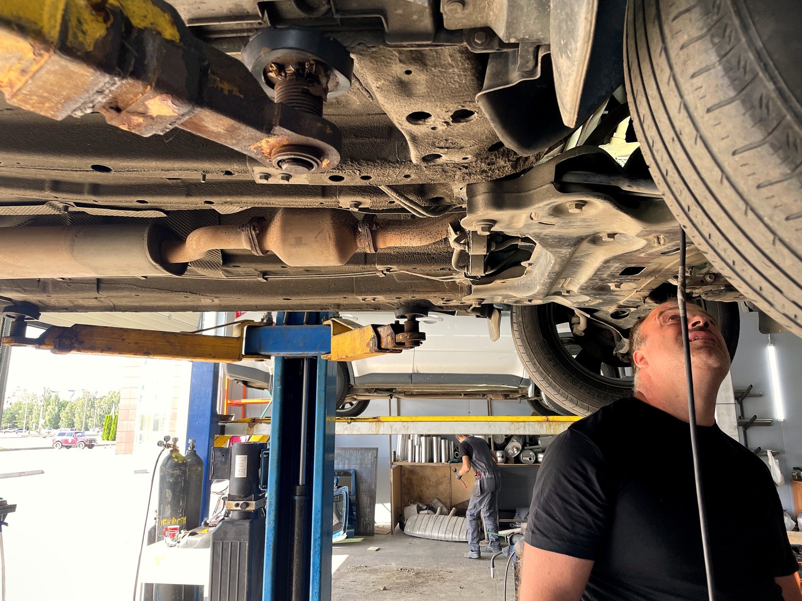 Днище белого кроссовера Chery на двухстоечном подъёмнике: выпускная линия в сборе, теплозащитный экран вдоль тоннеля
