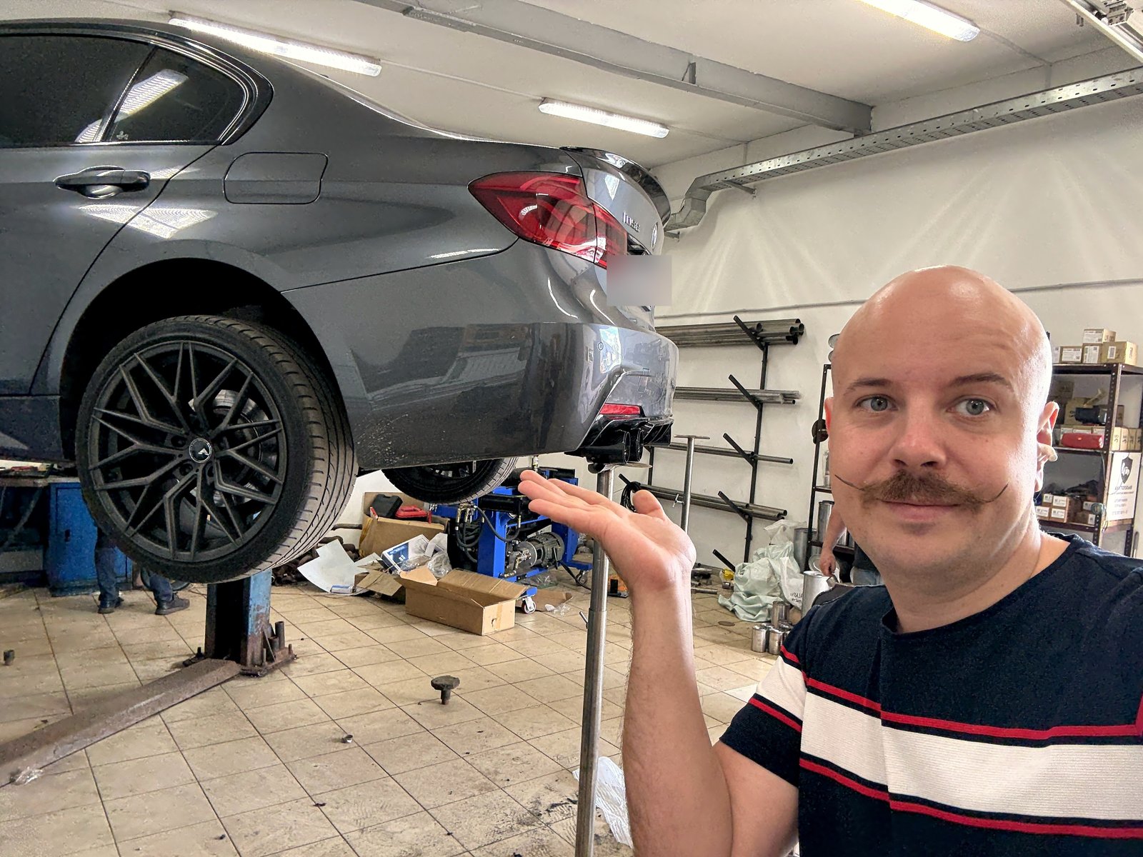 Серый седан BMW 320i на подъёмнике в цеху «Выхлопухи», задняя часть, чёрные диски