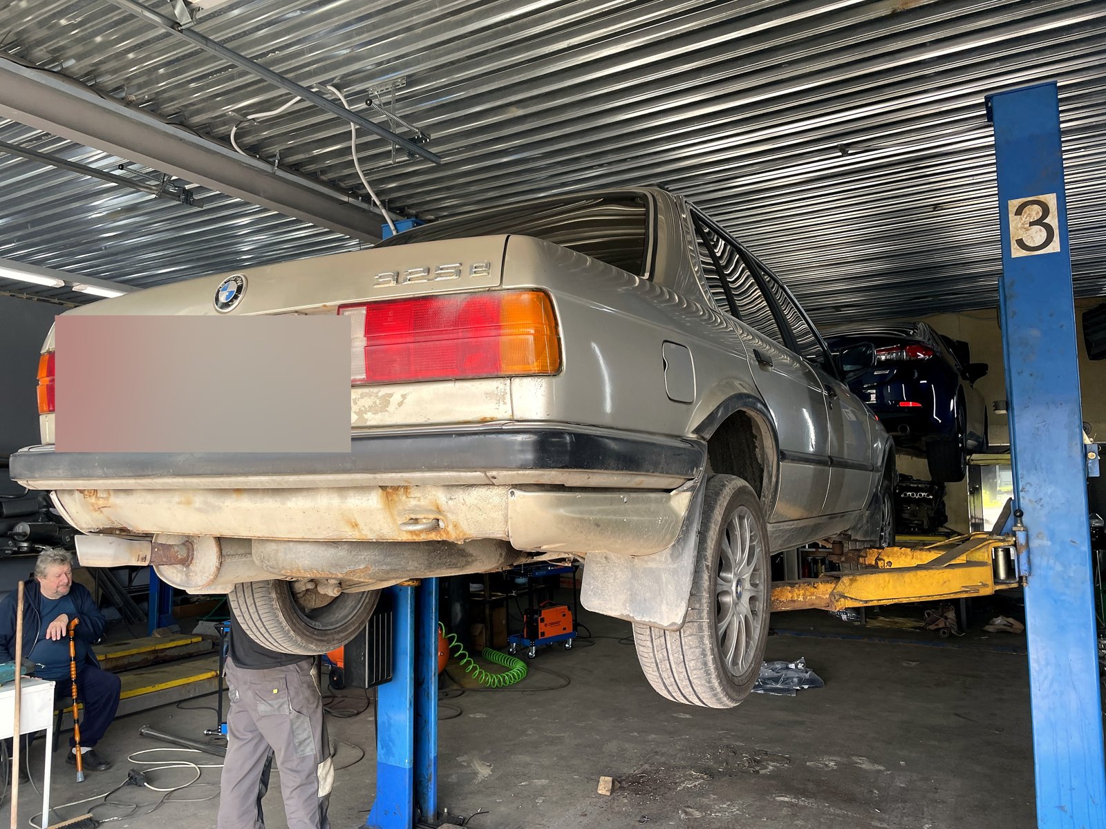 Крышка багажника BMW 325e в кузове E30 с шильдиком «325e», вид сзади на подъёмнике