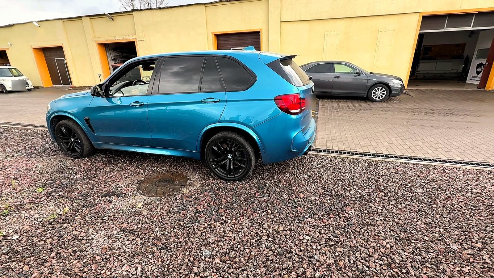 Синий BMW X5 M на улице у цеха «Выхлопухи», вид сзади сбоку