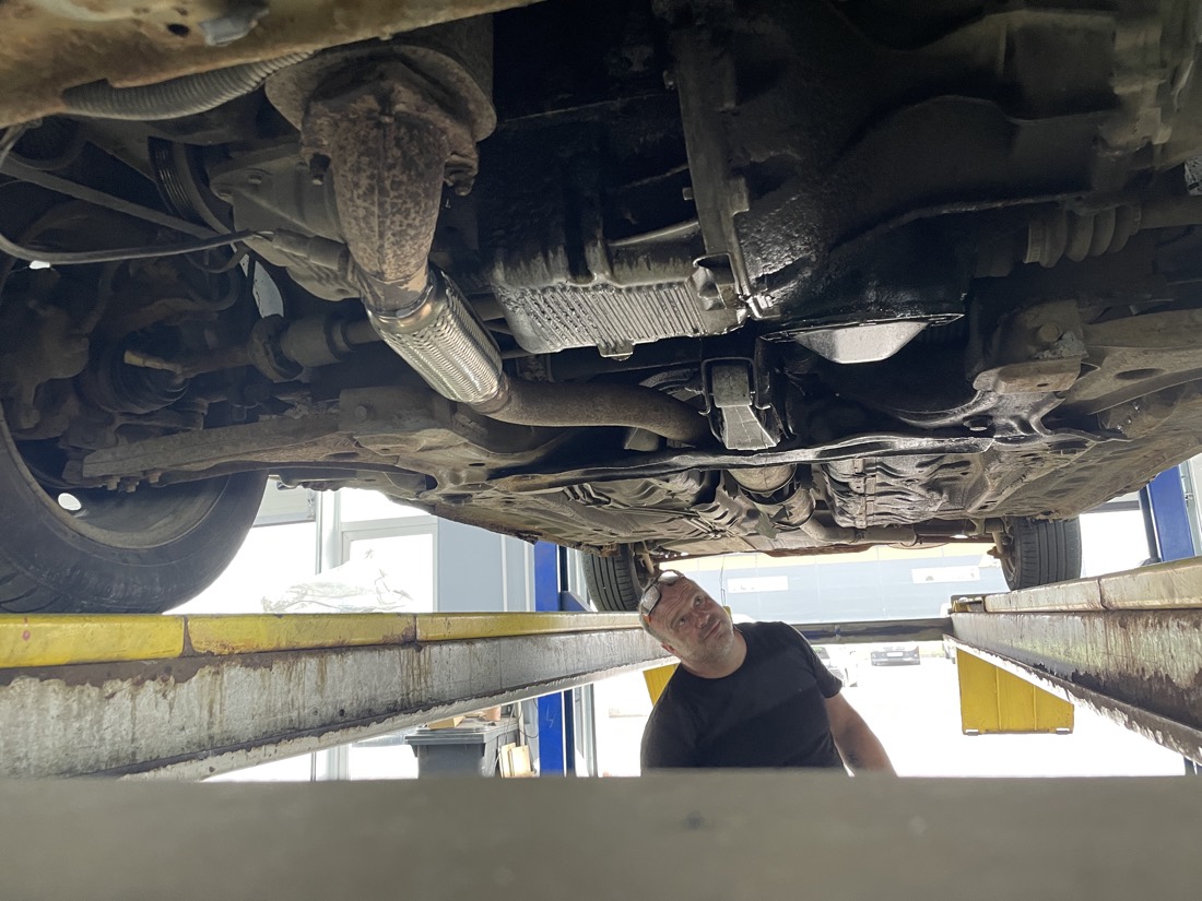 Выхлопная трасса Chevrolet Lacetti снизу после работы: новая гофра на месте, мастер осматривает машину на подъёмнике