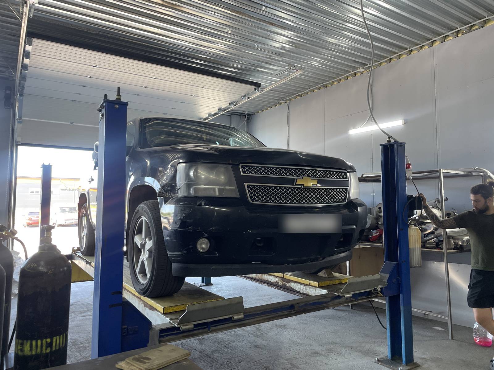 Чёрный Chevrolet Tahoe на подъёмнике в боксе «Выхлопухи», мастер осматривает выхлоп снизу