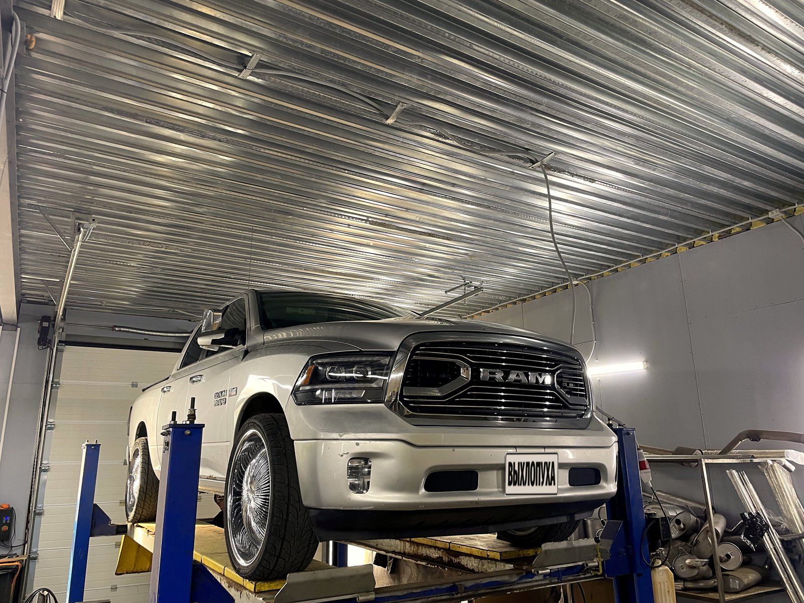 Серебристый пикап Dodge Ram на подъёмнике в боксе «Выхлопухи» в Тельмана, вид спереди, номер закрыт плашкой