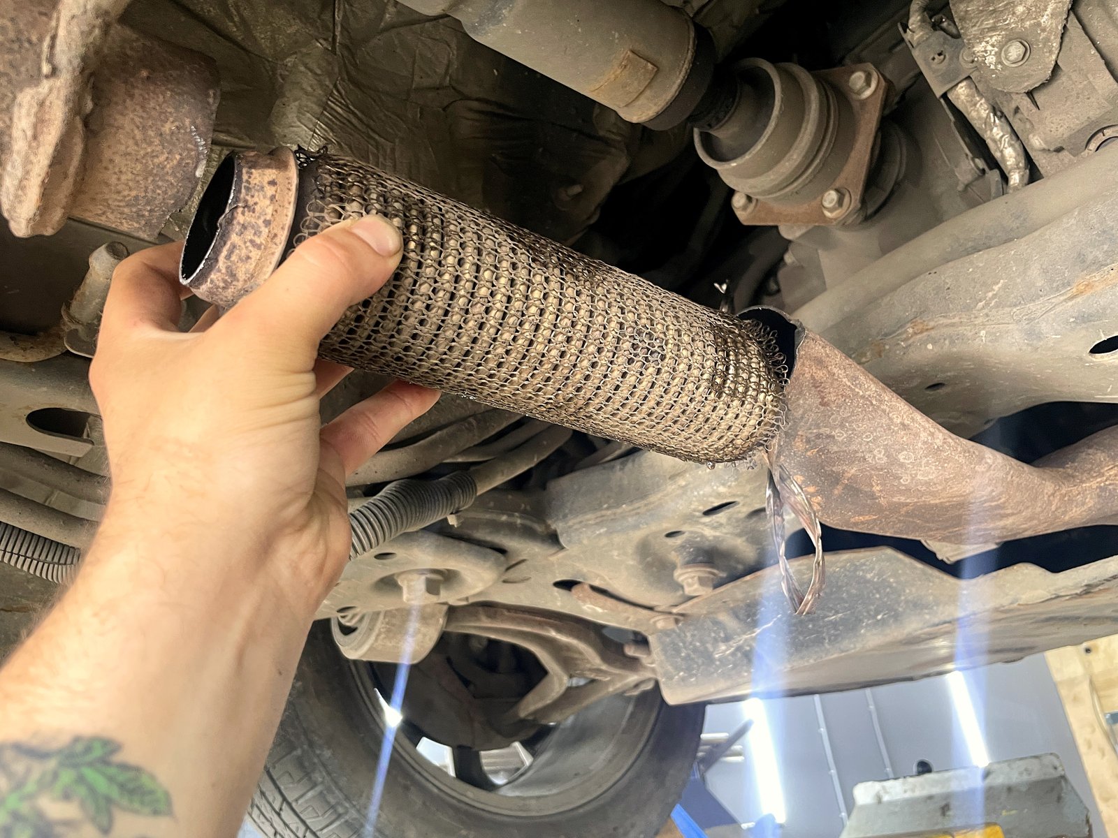 Мастер держит в руке вынутый порванный участок гофры Ford Explorer, крупный план дыры