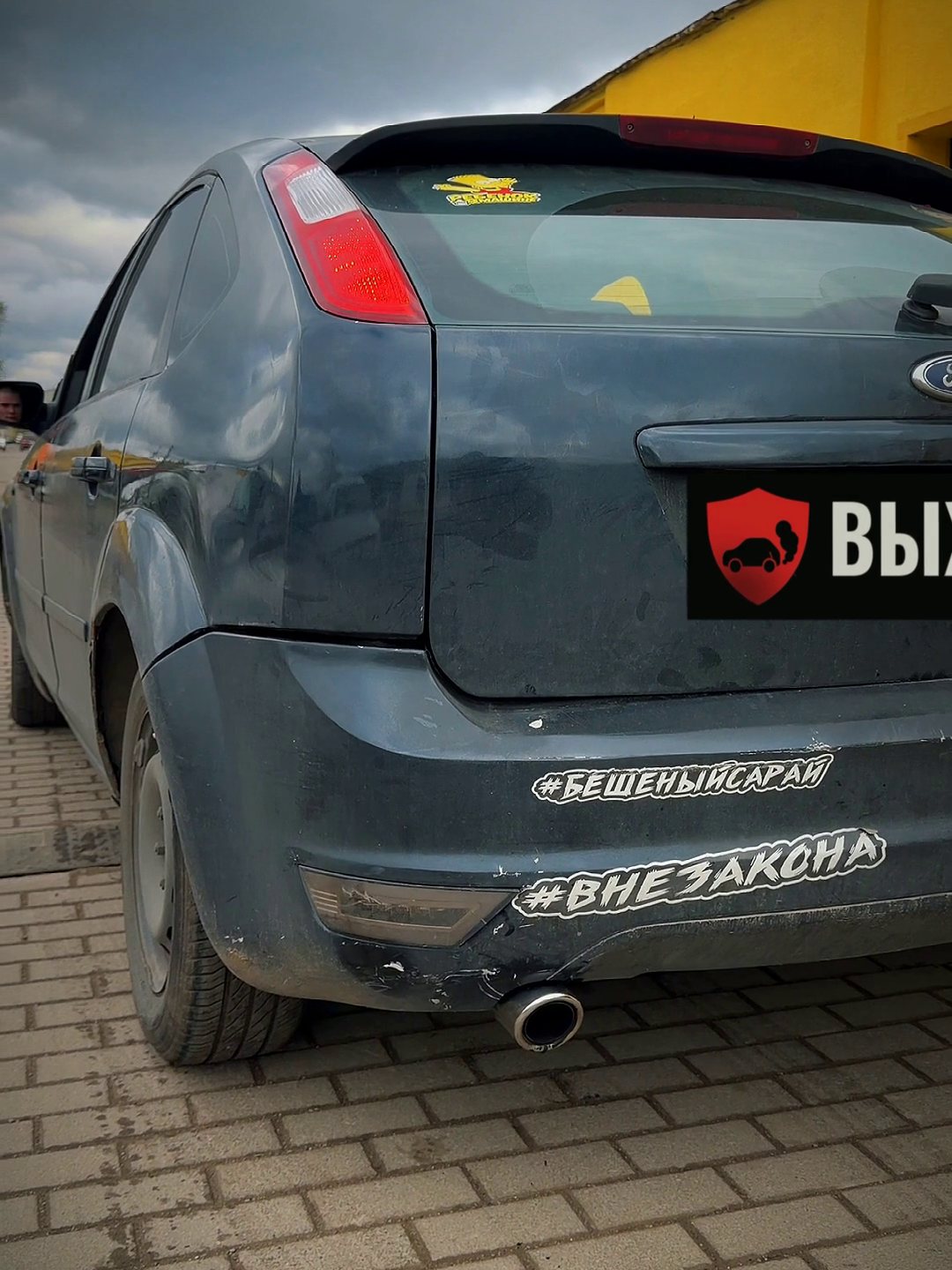 Тёмно-синий Ford Focus 2 сзади у жёлтых боксов «Выхлопухи», насадка слева, номер закрыт плашкой
