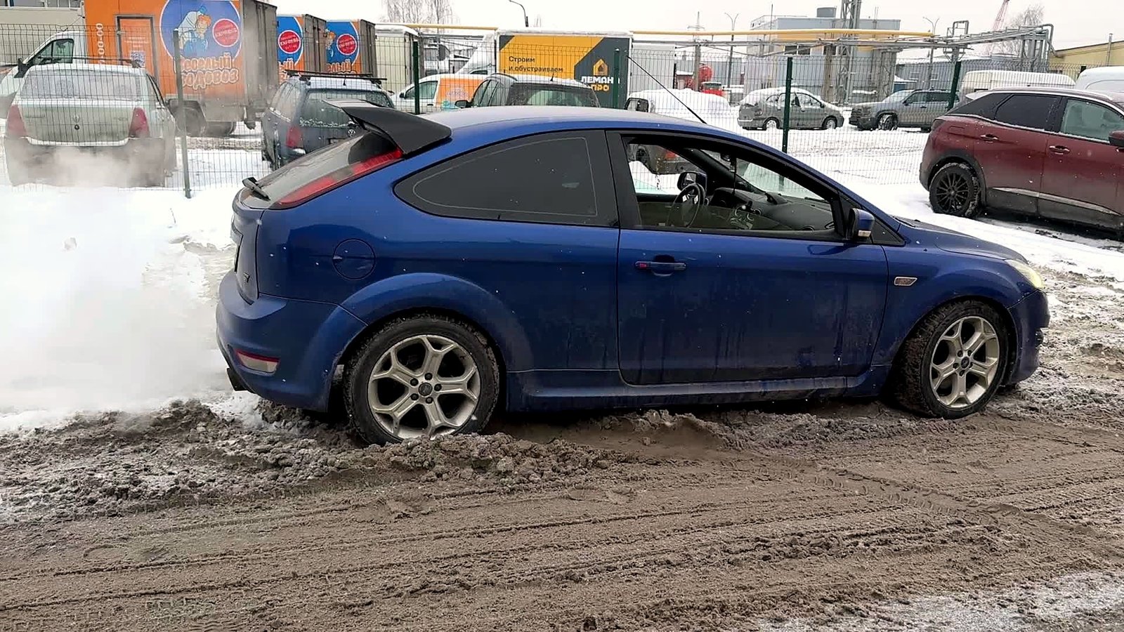 Синий трёхдверный Ford Focus ST на заснеженной площадке после работы, сзади из выхлопа идёт пар
