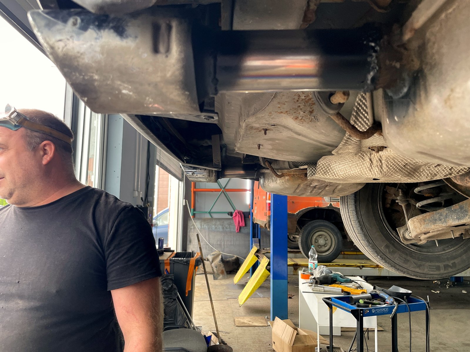 Вид снизу на левый задний глушитель Ford Mondeo 4: новый кусок трубы до насадки, рядом мастер «Выхлопухи»
