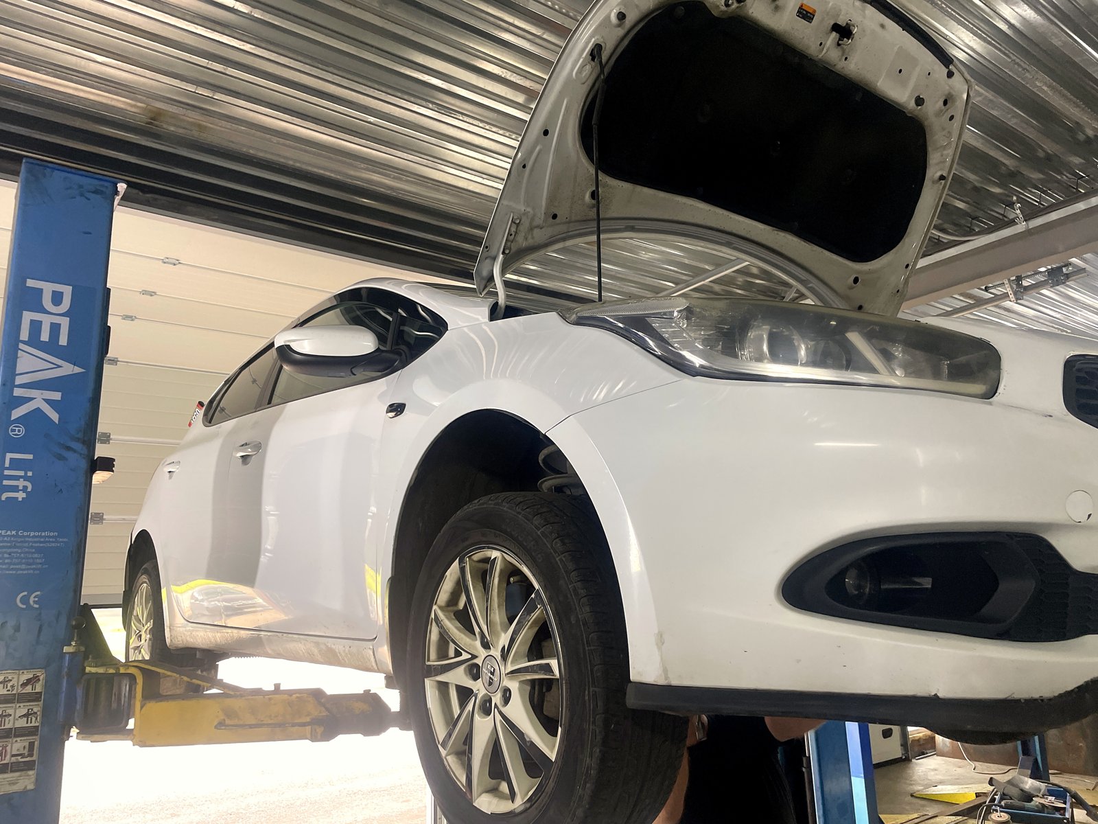 Белый Kia Ceed второго поколения сбоку на подъёмнике, капот открыт