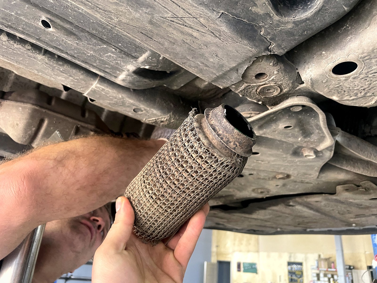 Снятая старая гофра Kia Ceed в руке мастера: оплётка разлохмачена, край патрубка рваный и ржавый