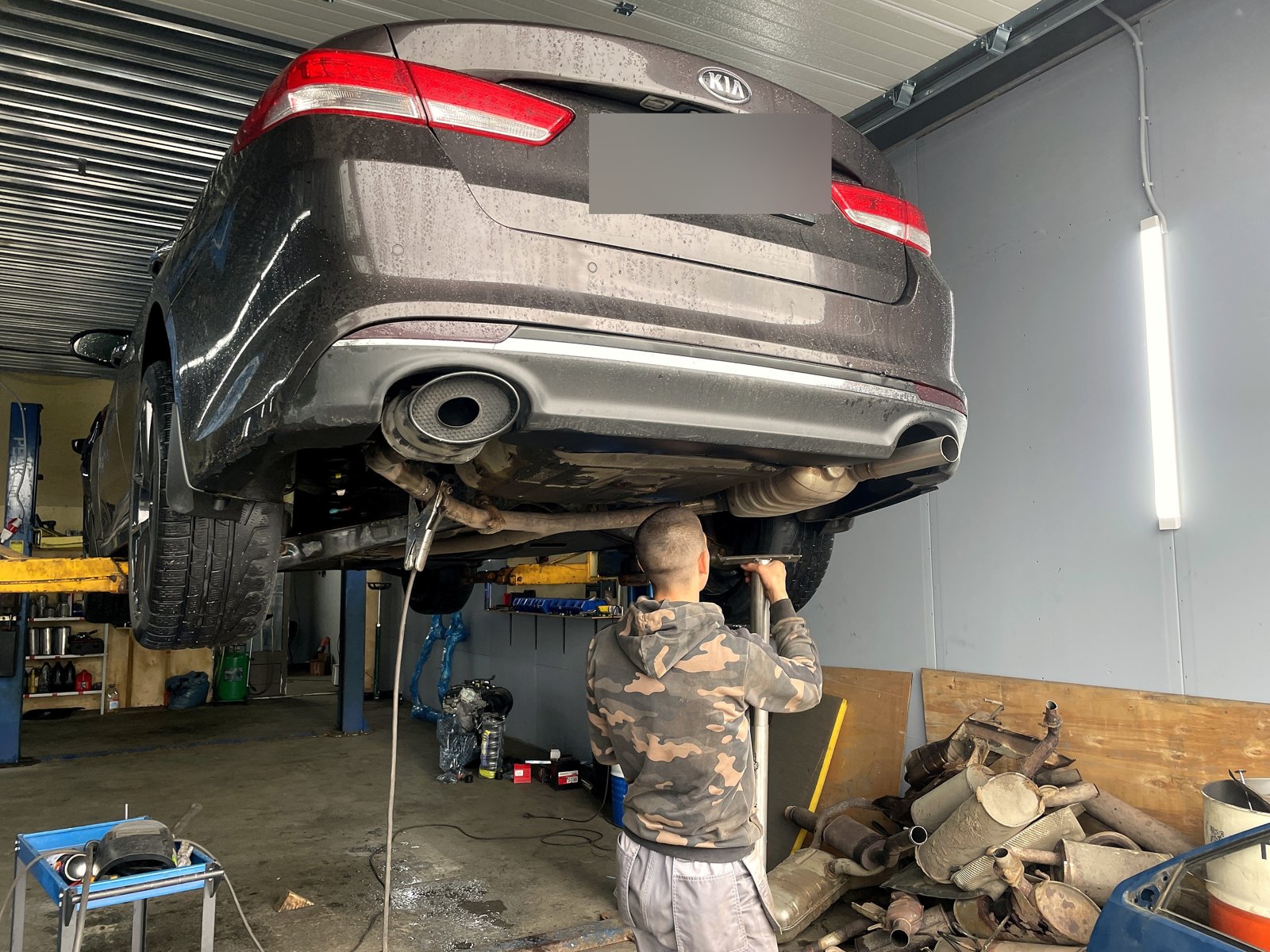 Задняя часть Kia Optima на подъёмнике снизу, выхлоп с двумя выходами, госномер замазан
