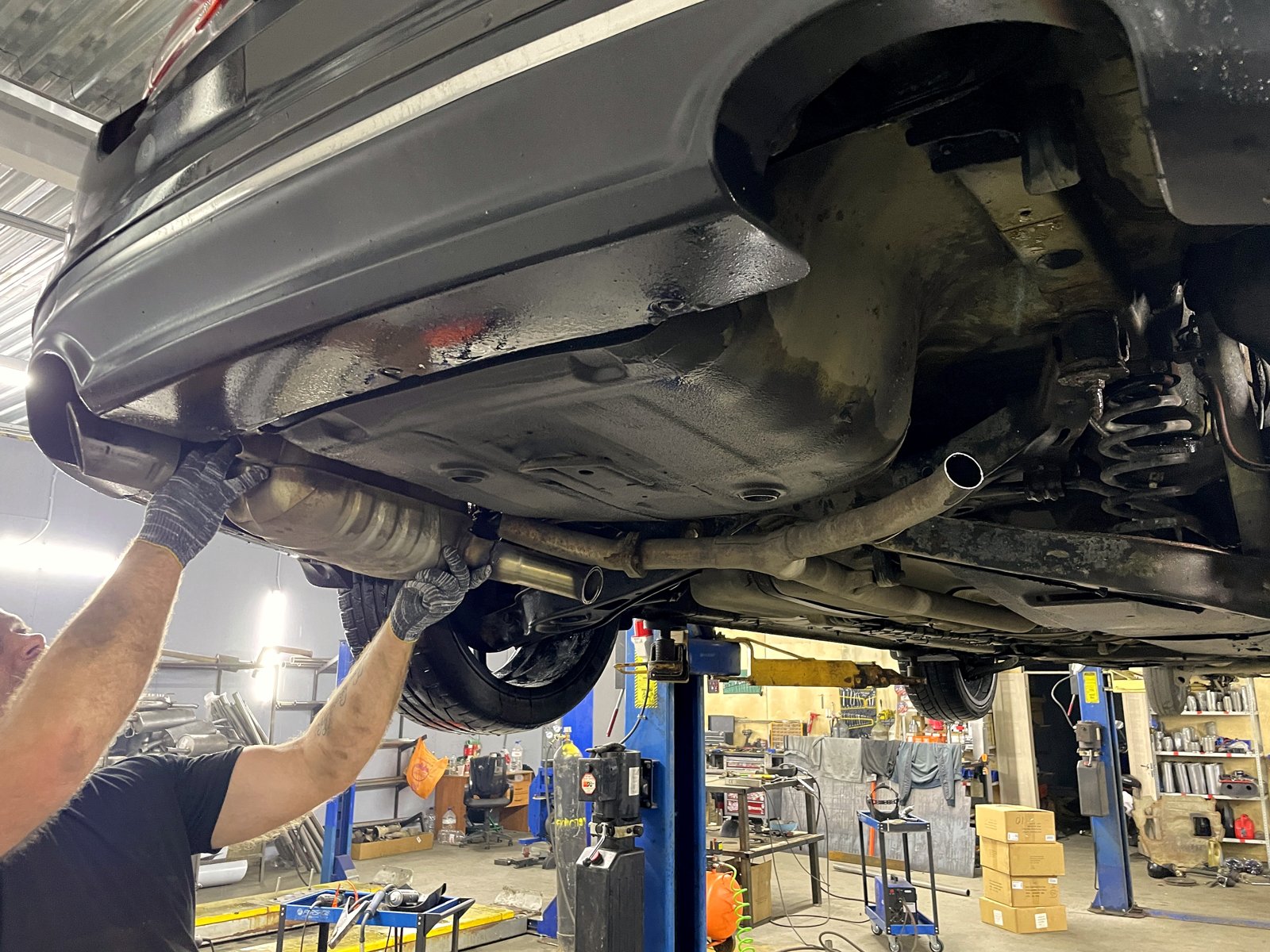Мастер «Выхлопухи» работает под днищем Kia на подъёмнике, снимает старый глушитель