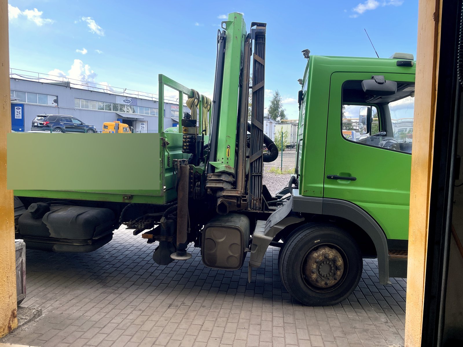 Зелёный грузовой Mercedes с манипулятором и бортовой платформой стоит у бокса «Выхлопухи»