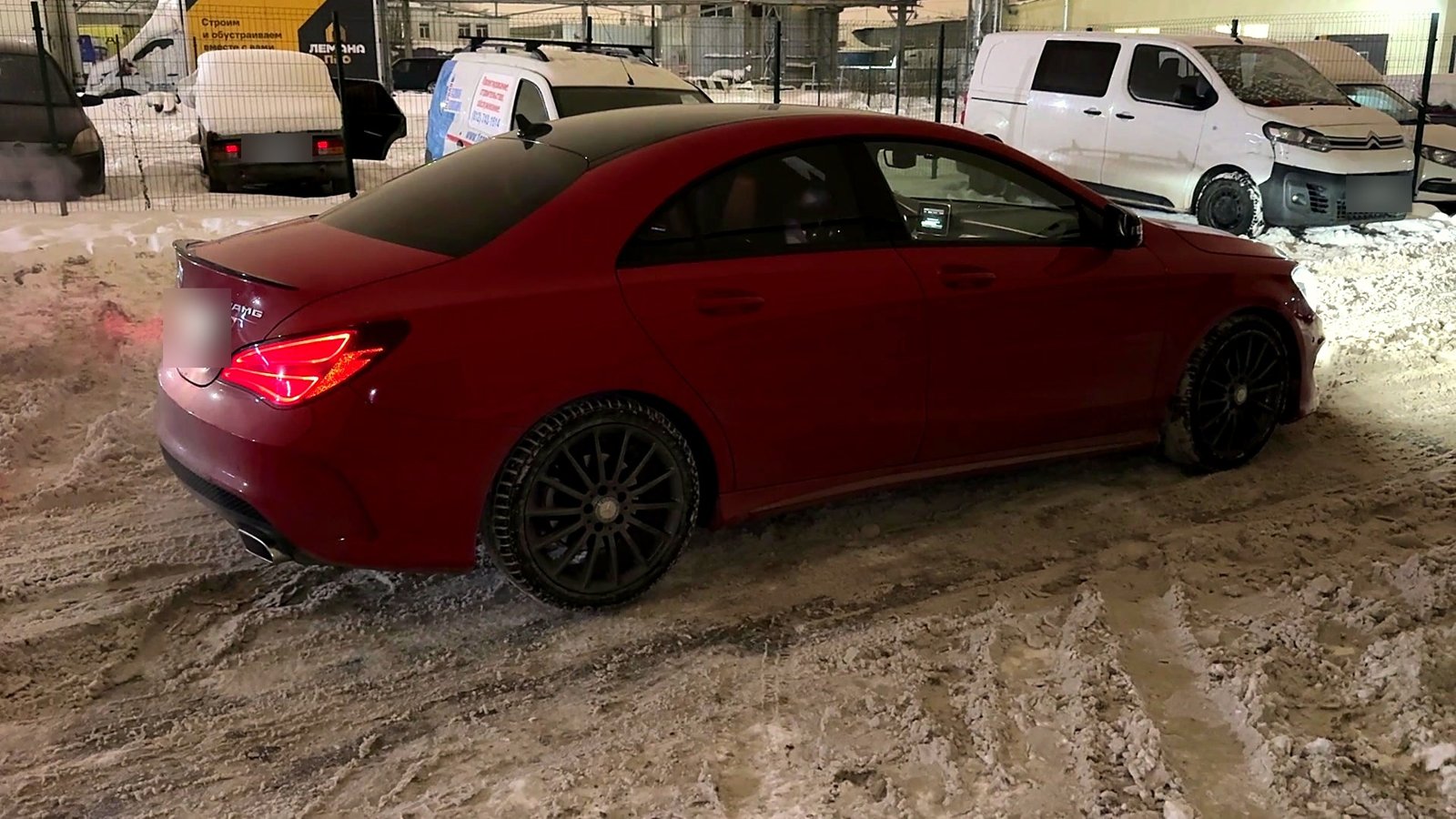 Красный Mercedes CLA на заснеженной площадке вечером, вид сзади сбоку, из выхлопа идёт пар