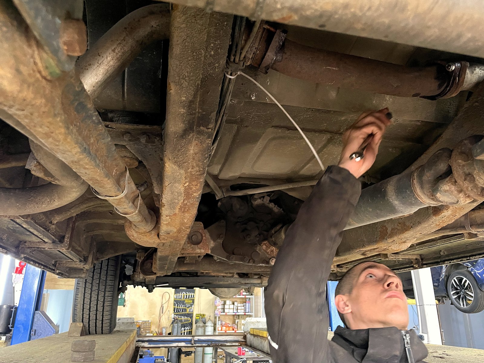 Мастер «Выхлопухи» с ключом под рамой Mercedes G-класс W463, видно старую выхлопную трассу и лонжероны в ржавчине
