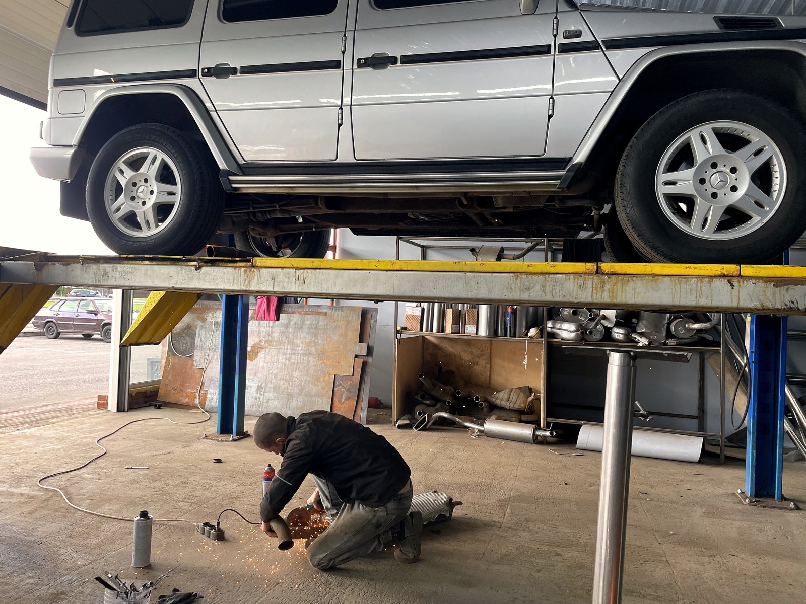 Мастер «Выхлопухи» режет трубу болгаркой на полу под Mercedes G-класс, летят искры