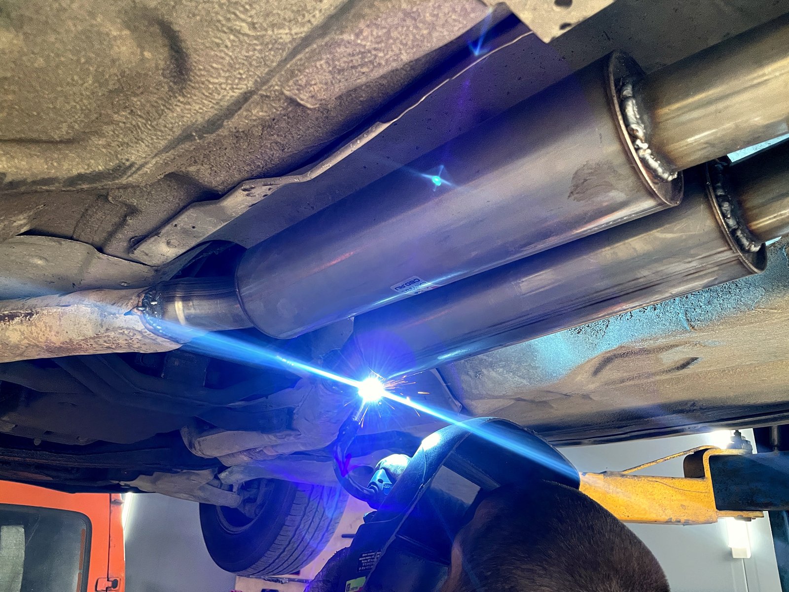Сварка стыка второго нержавеющего пламегасителя под днищем Mercedes W140, яркая дуга аргоновой сварки, рядом первый новый корпус