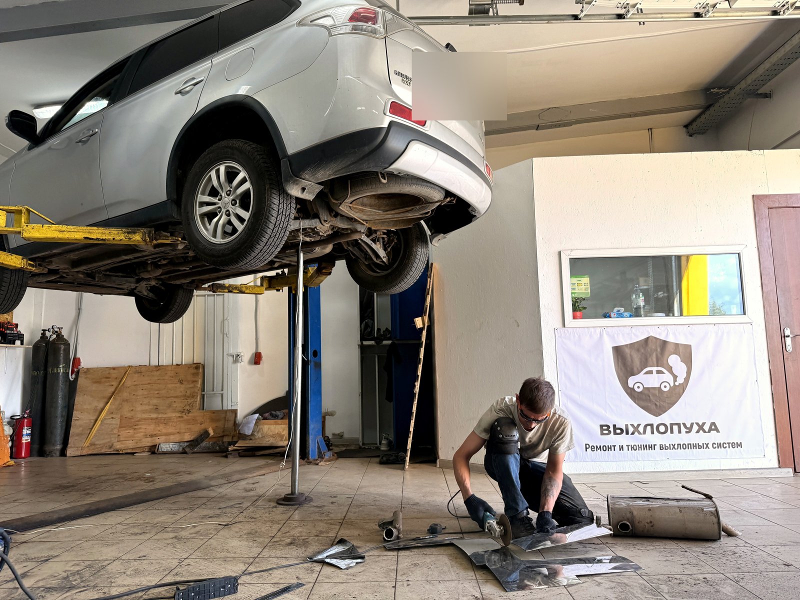 Белый Mitsubishi Outlander поднят на подъёмнике в цеху «Выхлопухи» на Южном шоссе