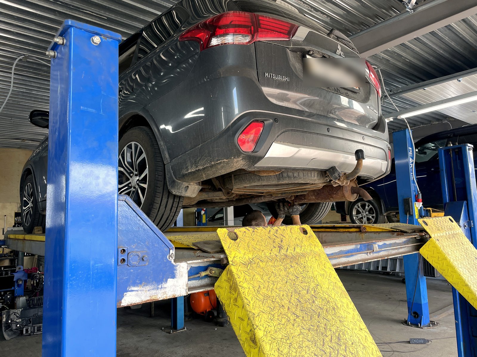 Тёмно-серый Mitsubishi Outlander поднят на подъёмнике в боксе «Выхлопухи», вид сзади