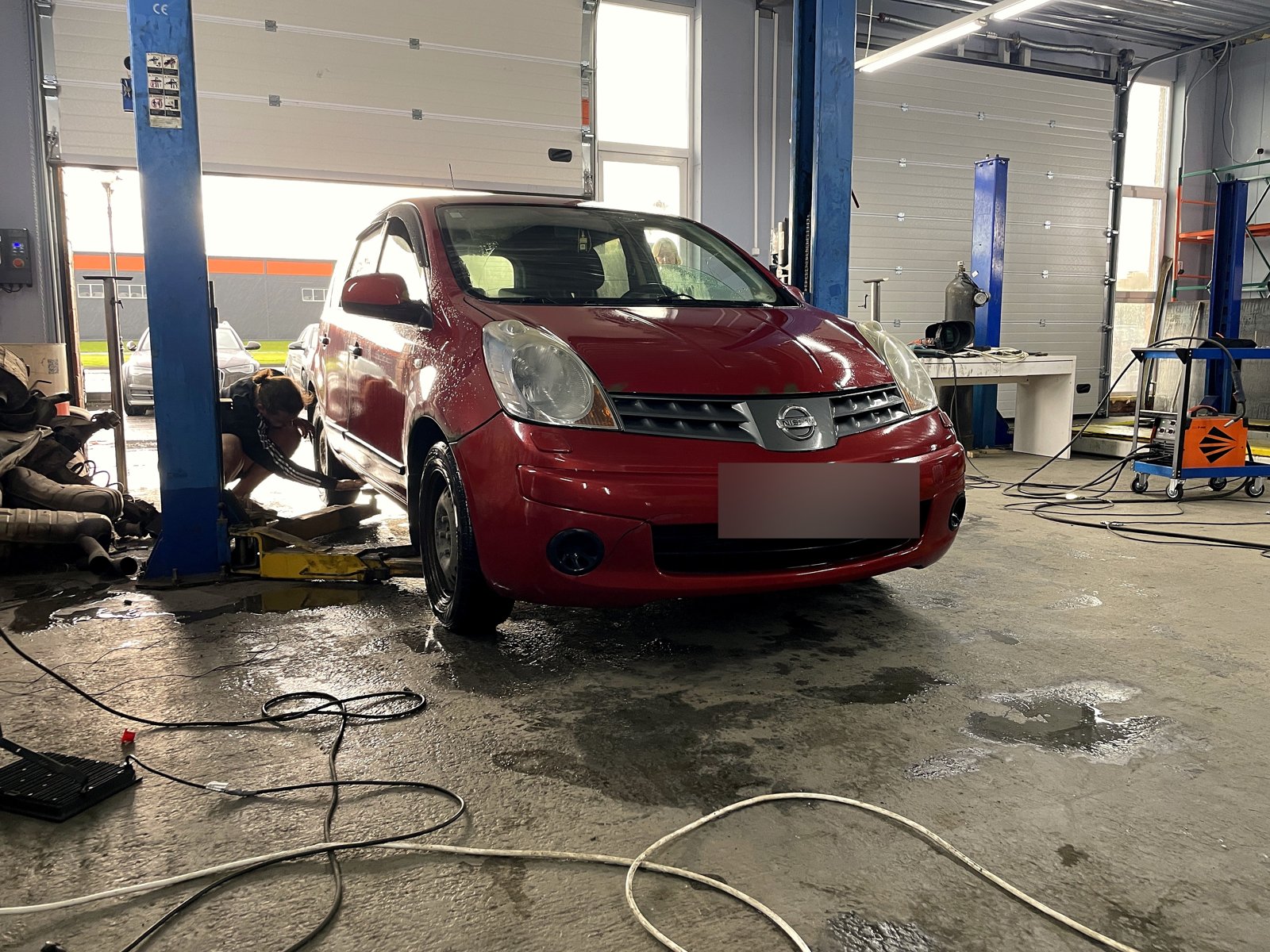 Красный Nissan Note в боксе «Выхлопухи» в Тельмана, вид спереди, госномер замазан