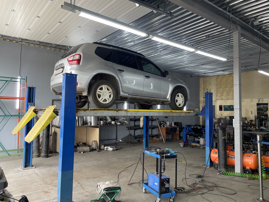Серебристый Nissan Terrano на подъёмнике в боксе «Выхлопухи», вид сзади сбоку