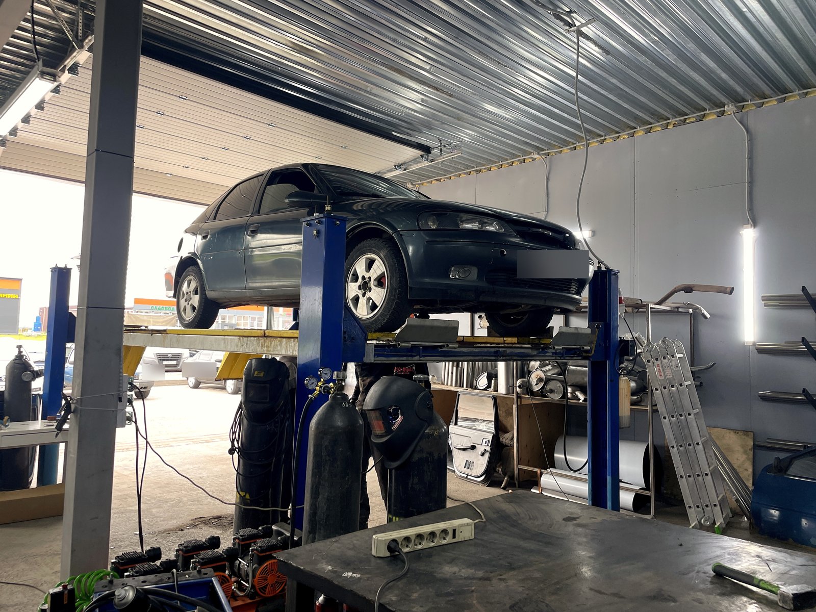Тёмный Opel Vectra B на подъёмнике в цехе «Выхлопухи», вид сбоку перед началом работы