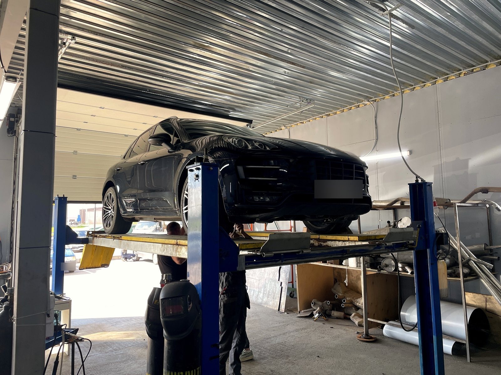 Чёрный Porsche Macan на четырёхстоечном подъёмнике в боксе «Выхлопухи», вид спереди, номер замазан