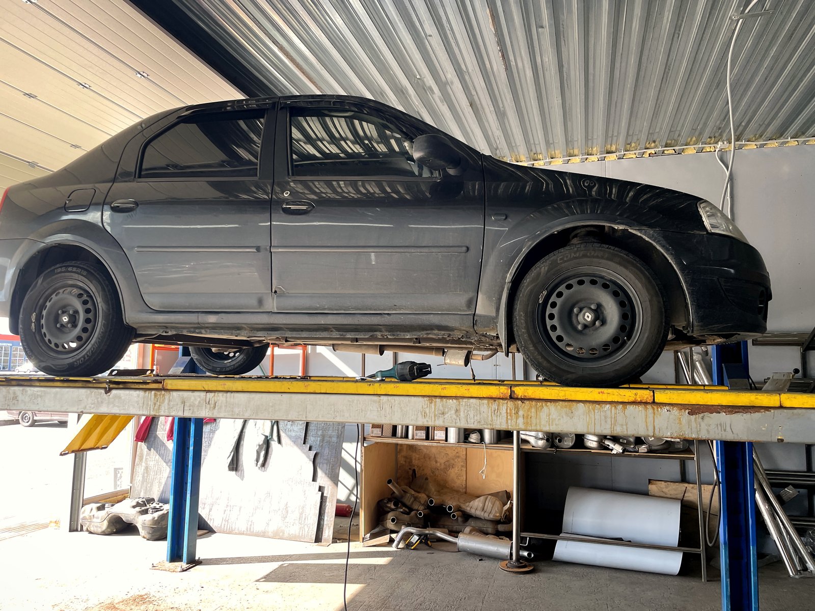 Тёмный Renault Logan первого поколения на подъёмнике в цехе «Выхлопухи» на Тельмана