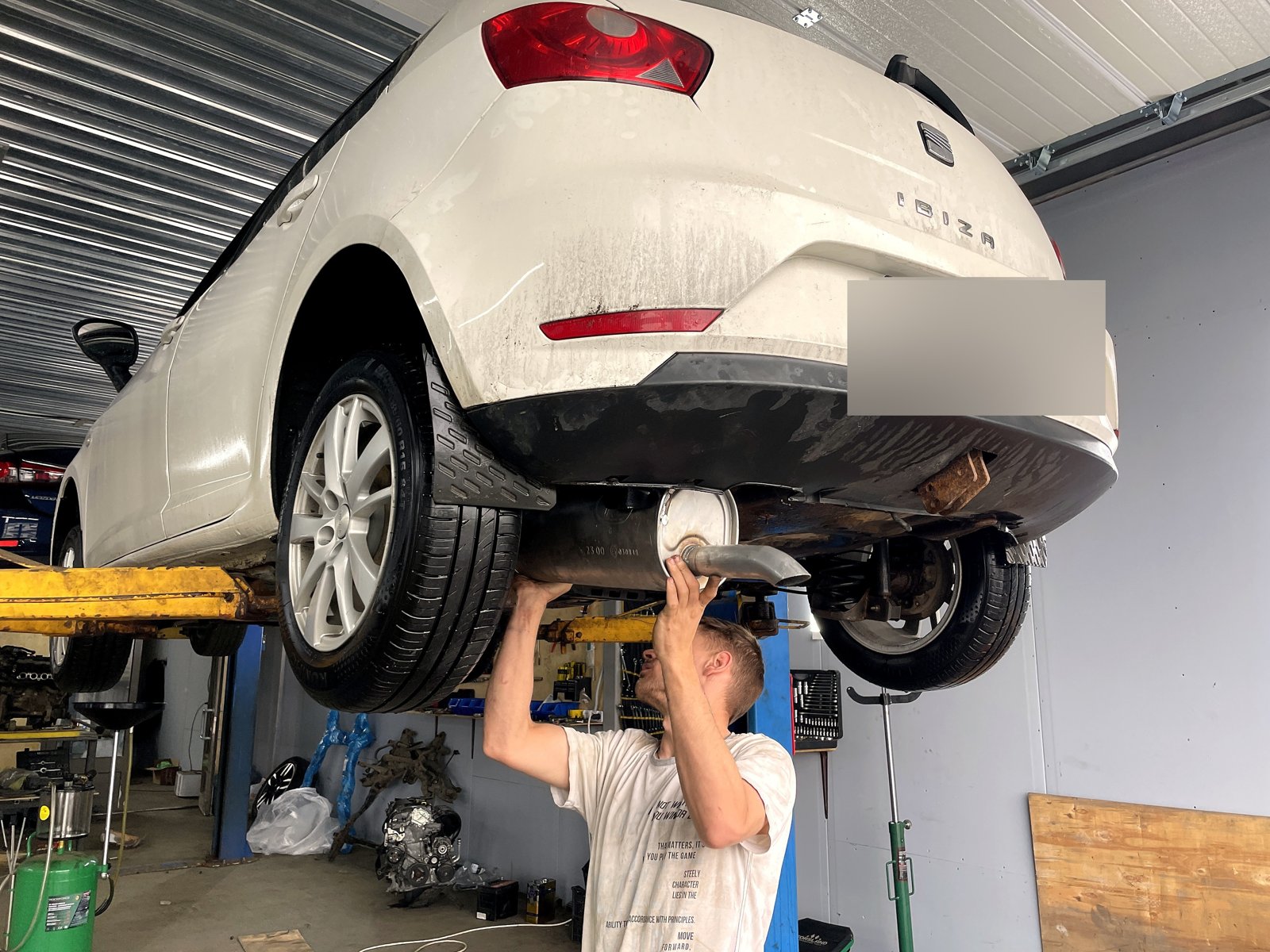 Вид снизу на заднюю часть SEAT Ibiza, мастер работает под днищем, задний номер замазан