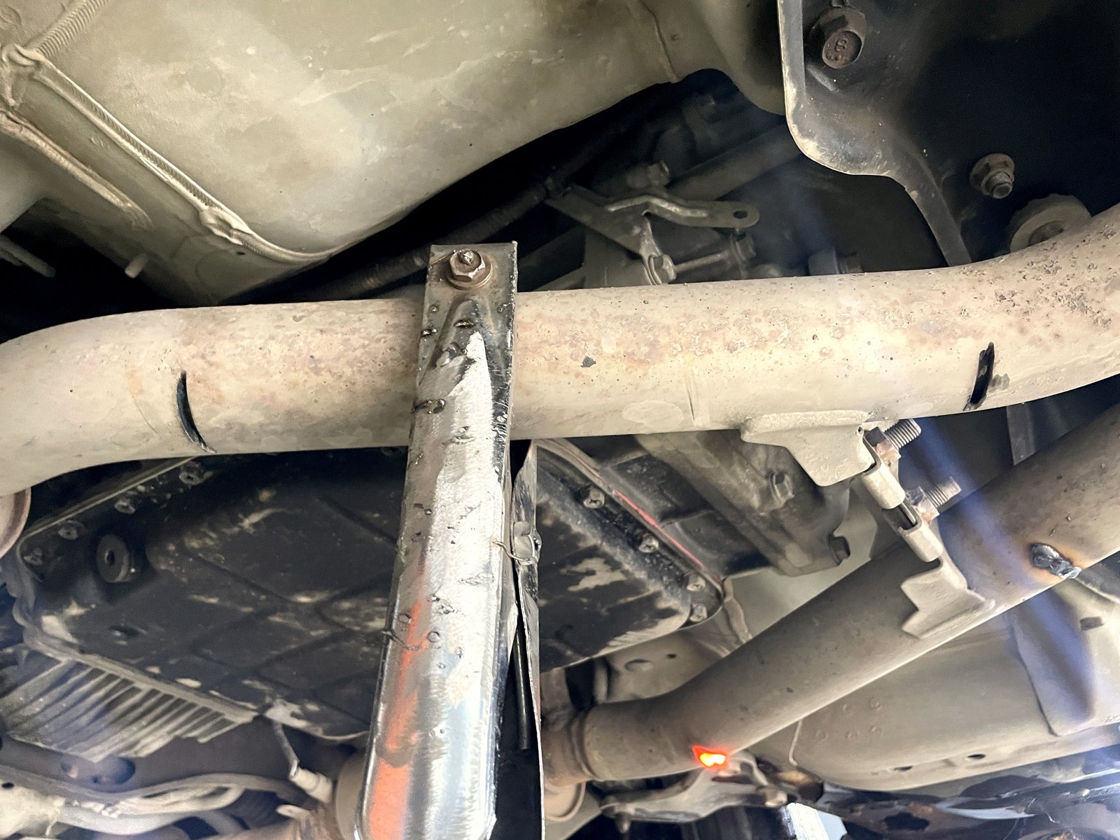 Приёмная труба Subaru Outback снизу с прорезями в наружном слое, рядом упор подъёмника