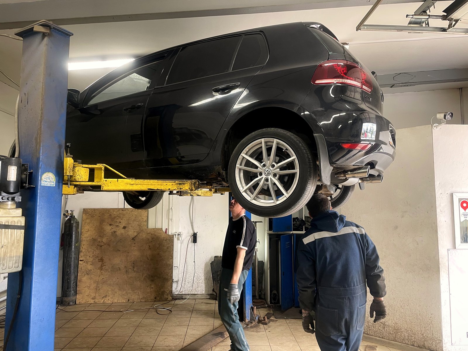 Чёрный Volkswagen Golf поднят на подъёмнике в боксе «Выхлопухи», вид сзади сбоку