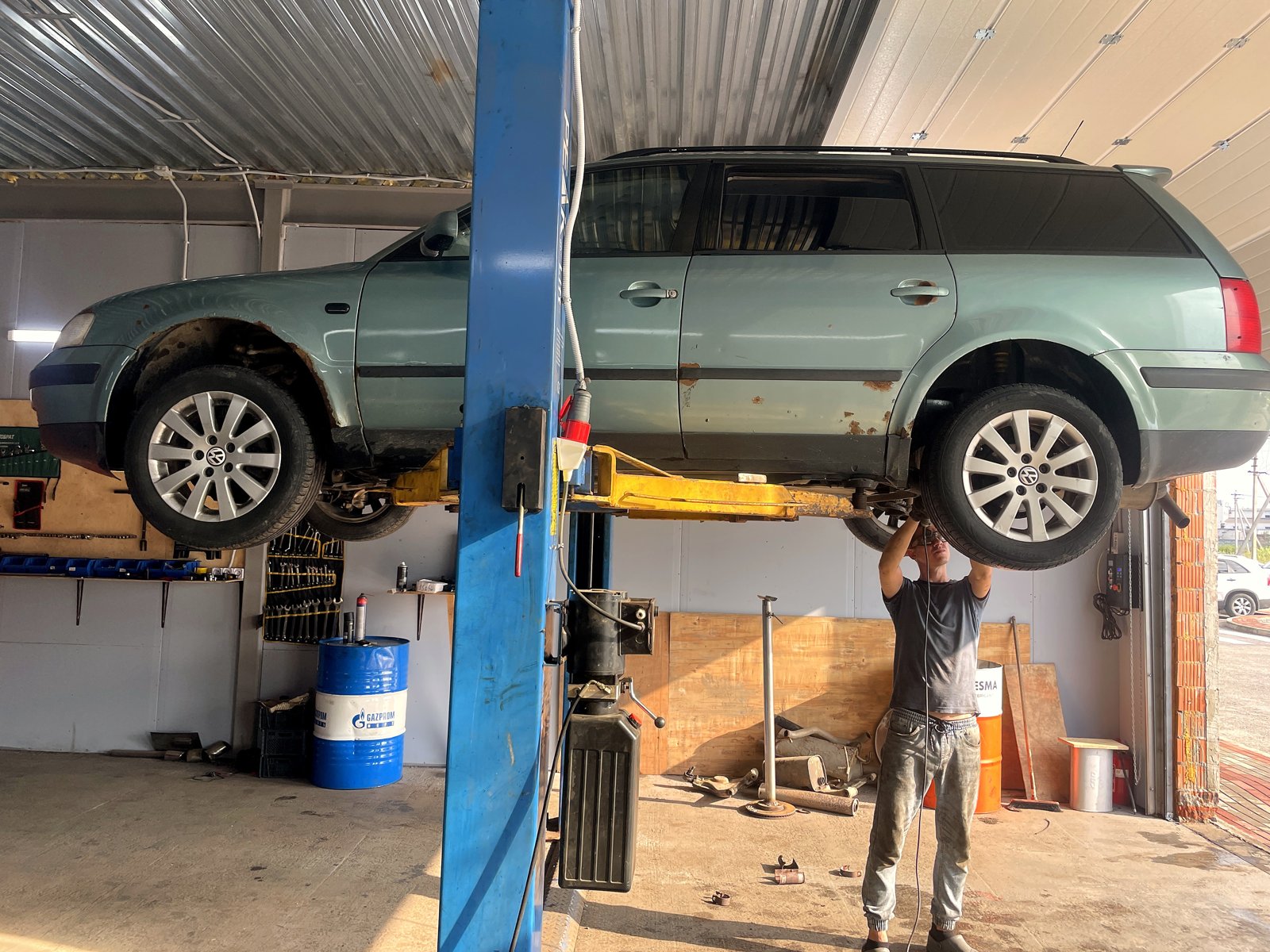 VW Passat B5 универсал поднят на подъёмнике в боксе «Выхлопухи», мастер стоит под днищем