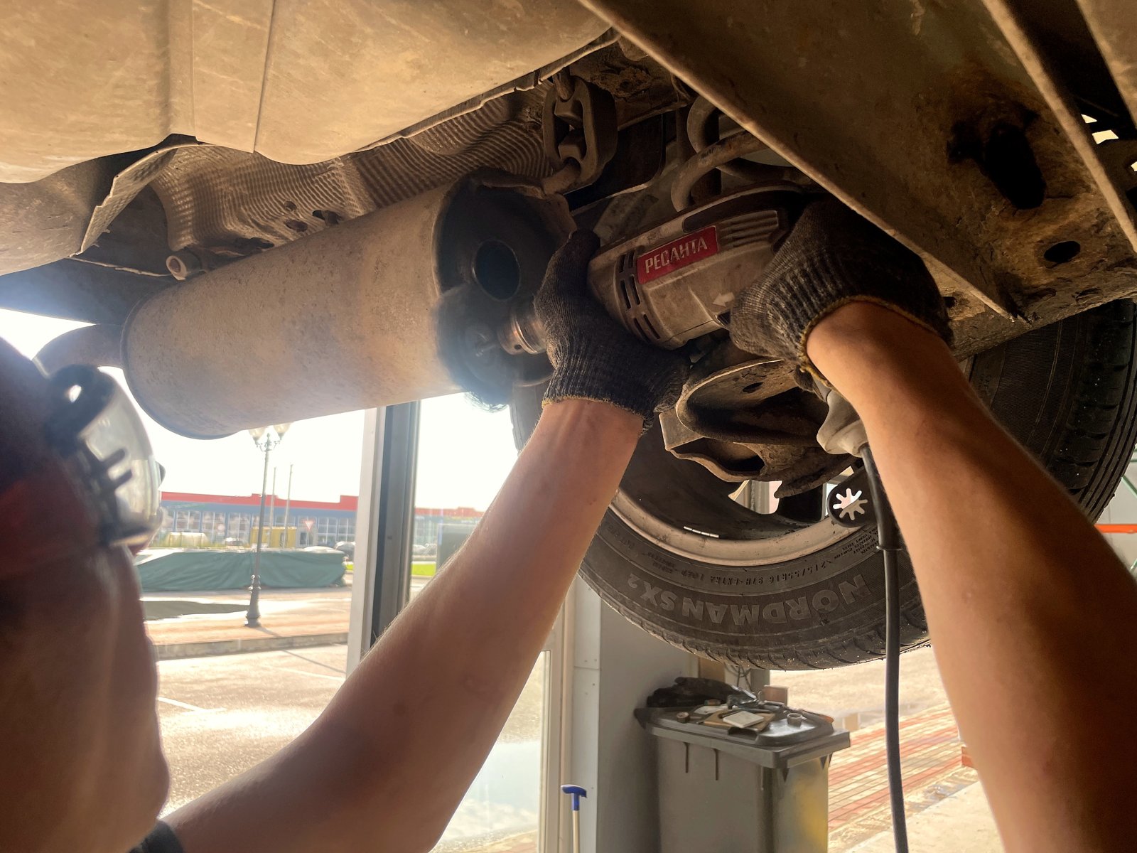 Мастер срезает старую выхлопную трубу болгаркой под днищем VW Passat B5