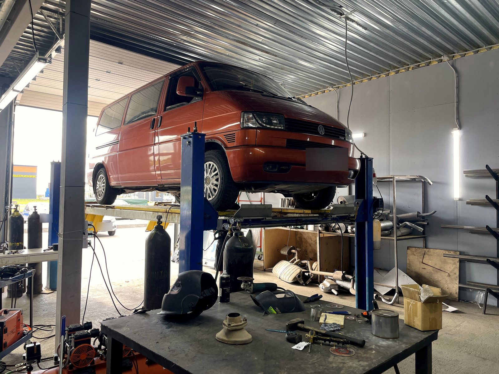 Терракотовый Volkswagen Transporter T4 на двухстоечном подъёмнике в боксе «Выхлопухи», номер замазан