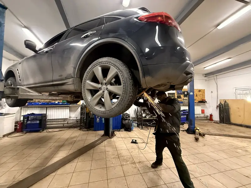 Тёмно-серый Infiniti FX35 на подъёмнике в цеху «Выхлопухи», под задней частью мастер срезает штатный выхлоп