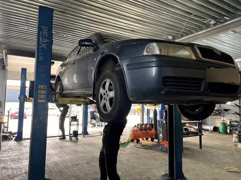 Тёмно-синяя Škoda Octavia первого поколения поднята на двухстоечном подъёмнике в боксе «Выхлопухи», вид спереди-сбоку