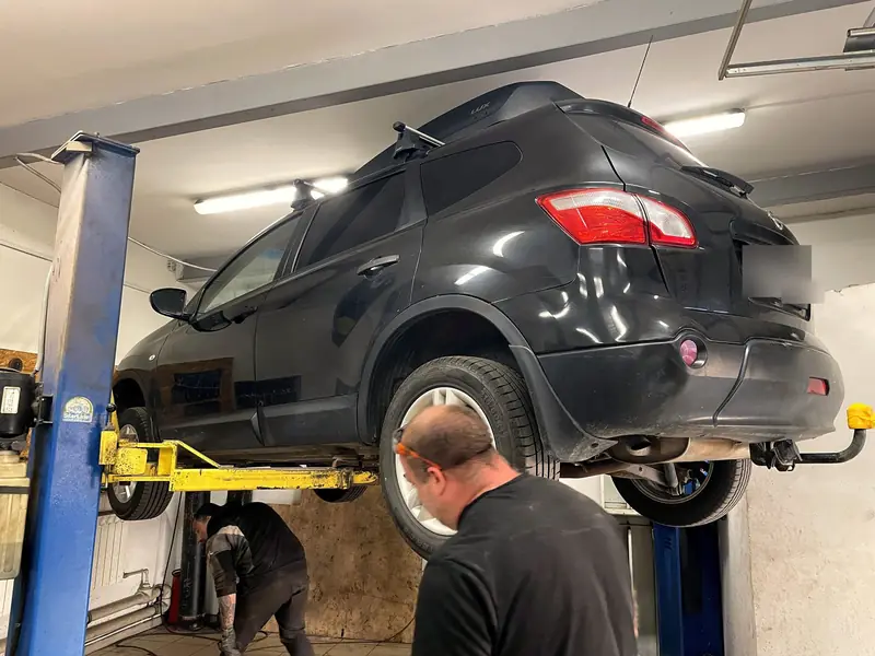 Чёрный Nissan Qashqai поднят на подъёмнике в боксе «Выхлопухи», вид сзади-сбоку