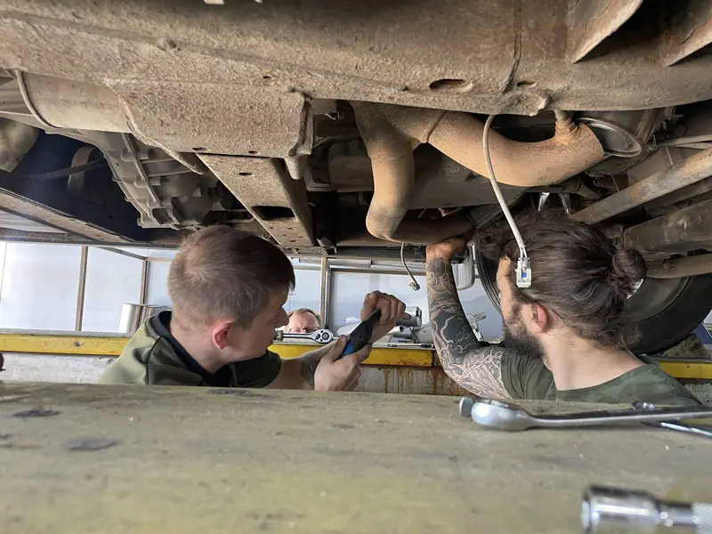 Два мастера «Выхлопухи» осматривают выхлопную систему Chevrolet Tahoe снизу на подъёмнике