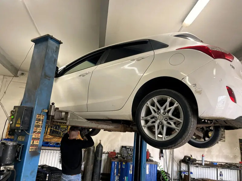 Белый Hyundai i30 на подъёмнике в боксе «Выхлопухи» на Южном шоссе, мастер осматривает днище