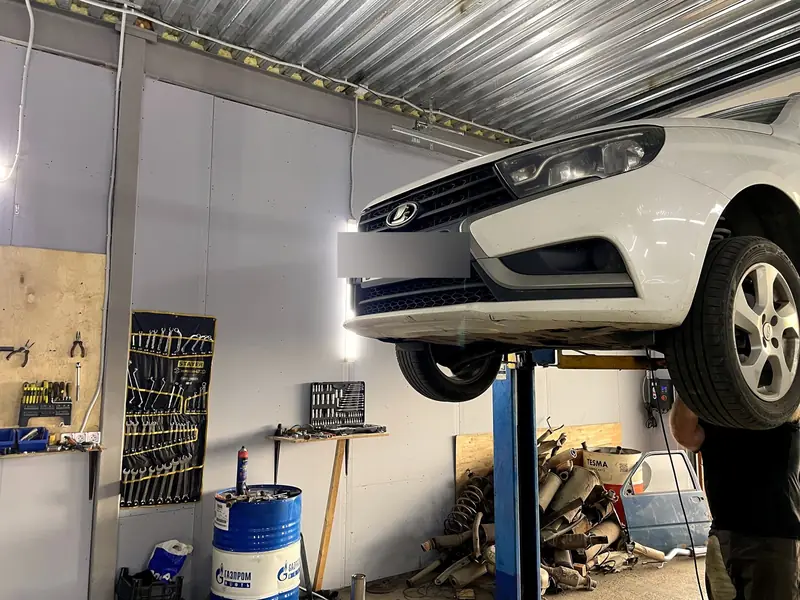 Белая Lada Vesta на подъёмнике в боксе «Выхлопухи» в Тельмана, вид спереди, госномер замазан