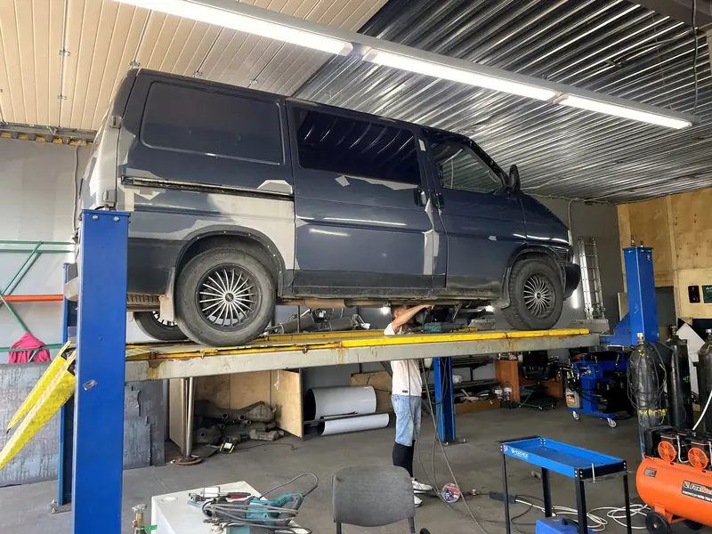 Синий Volkswagen Transporter на двухстоечном подъёмнике в боксе «Выхлопухи»