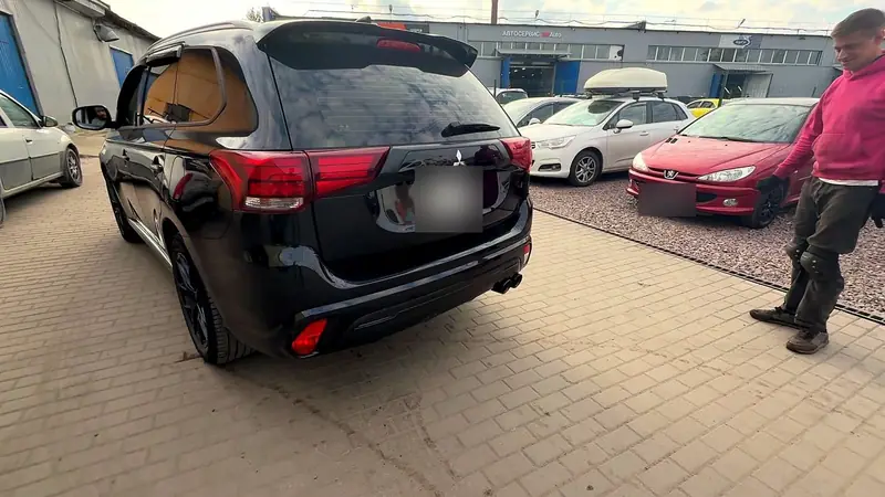 Чёрный Mitsubishi Outlander у цеха «Выхлопухи», вид сзади сбоку, из бампера торчат сдвоенные насадки