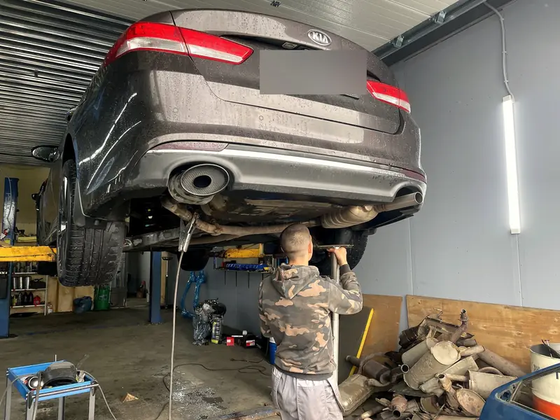 Задняя часть Kia Optima на подъёмнике снизу, выхлоп с двумя выходами, госномер замазан
