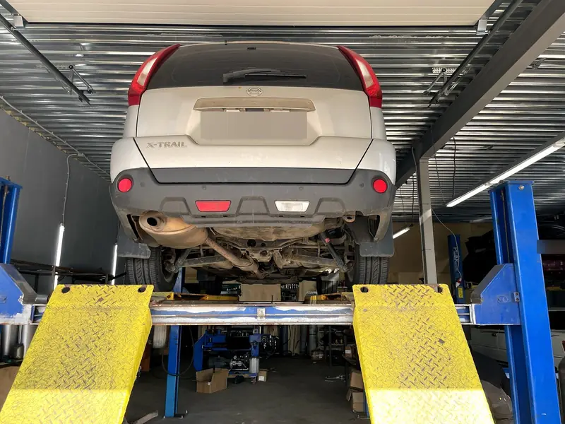 Корма Nissan X-Trail на двухстоечном подъёмнике в боксе, снизу видна задняя банка глушителя, номер замазан