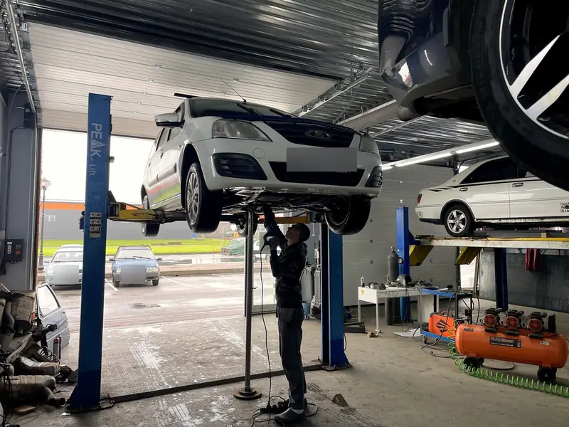 Белая Lada Largus на подъёмнике в боксе «Выхлопухи» в Тельмана, госномер замазан