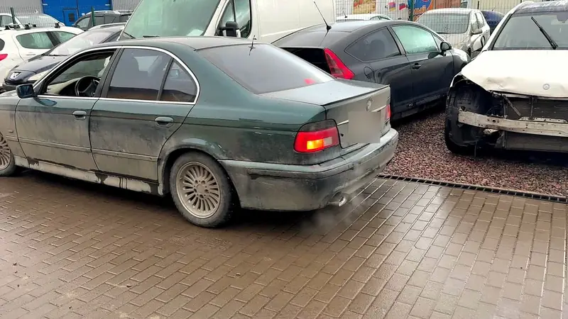 Тёмно-зелёный BMW 5 E39 на площадке после работы, вид сзади сбоку, у насадки пар от выхлопа
