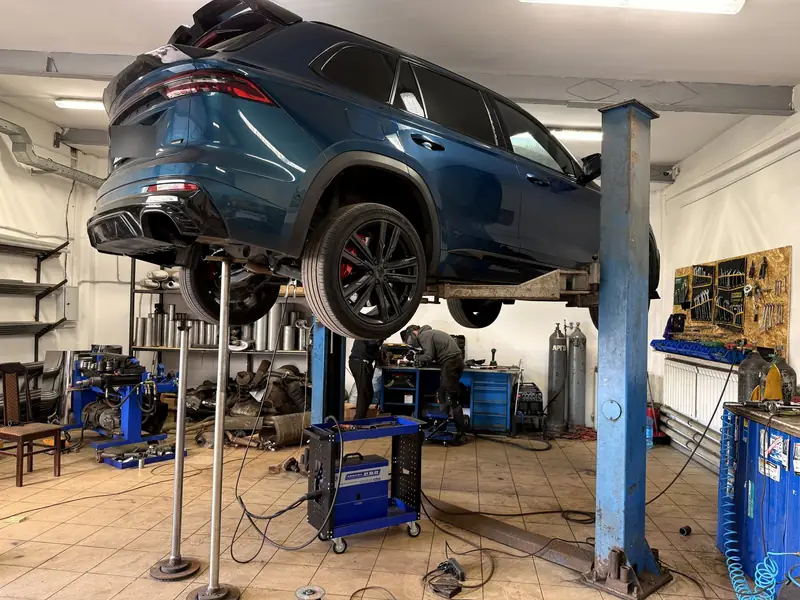 Синий кроссовер Geely Monjaro на подъёмнике в цеху «Выхлопухи», задняя часть, диффузор бампера без насадок